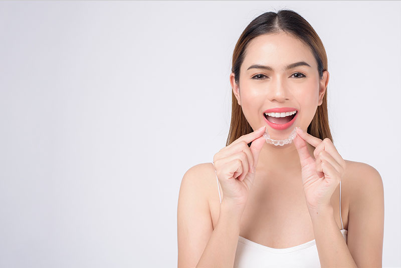 Young smiling woman holding invisalign braces in studio, dental healthcare and Orthodontic concept