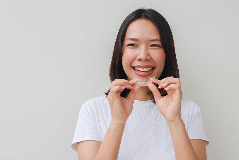 close up young asian woman smiling with hand holding dental aligner retainer