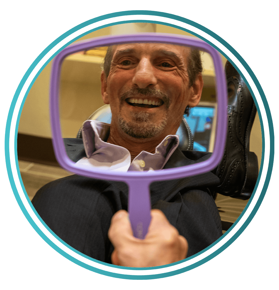 patient smiling brightly after their dental treatment looking within a handheld mirror