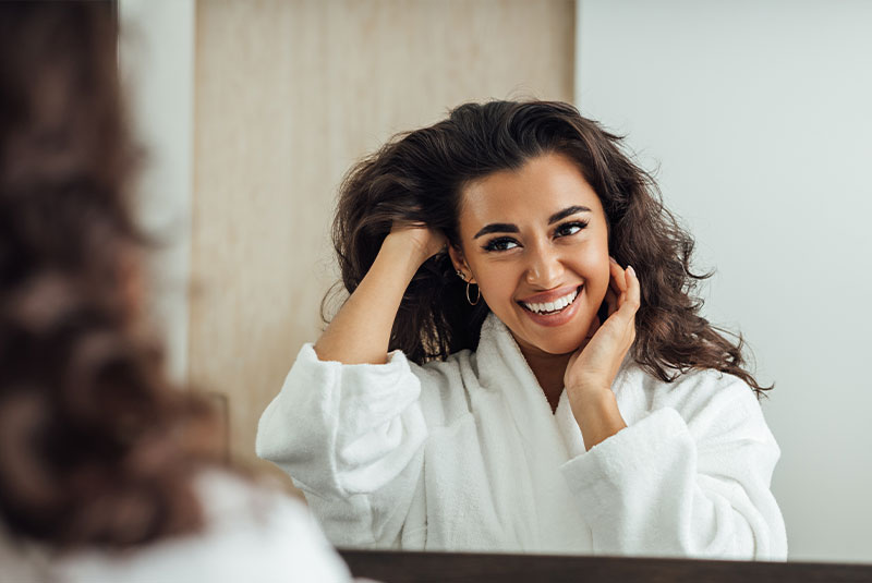 beautiful young model smiling brightly while looking at themselves within the bathroom mirror
