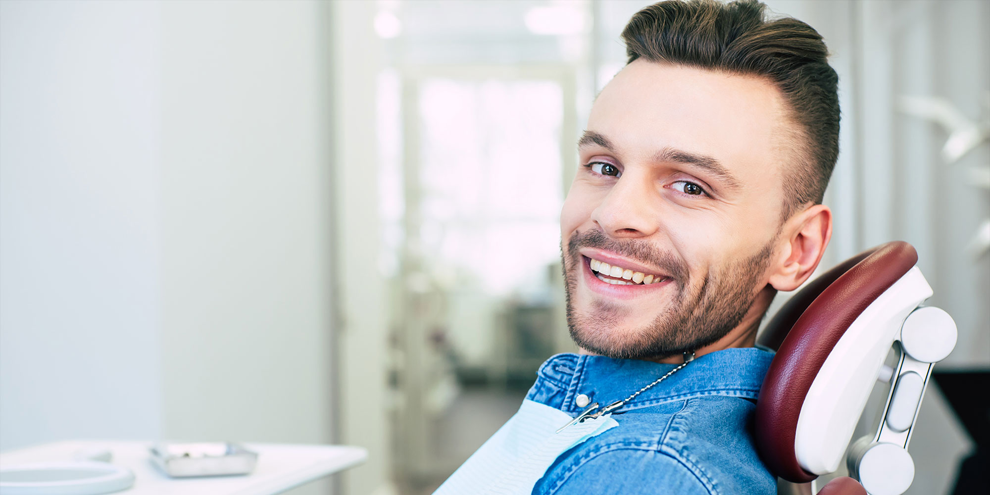 Happy man with hazel eyes and dark brown hair is sitting in dental chair and smiling